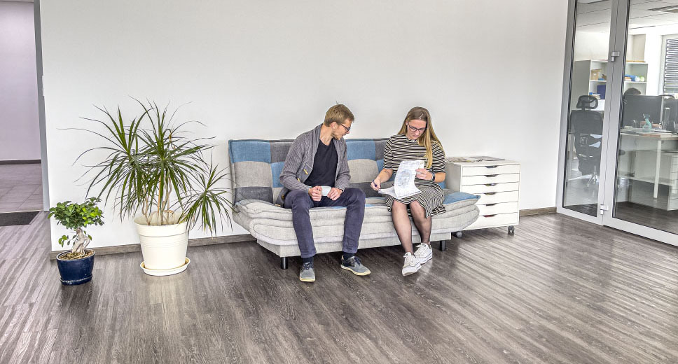 Two colleagues sitting on a comfortable couch in a modern office space at IGM. Behind them, live plants add a natural touch to the environment.